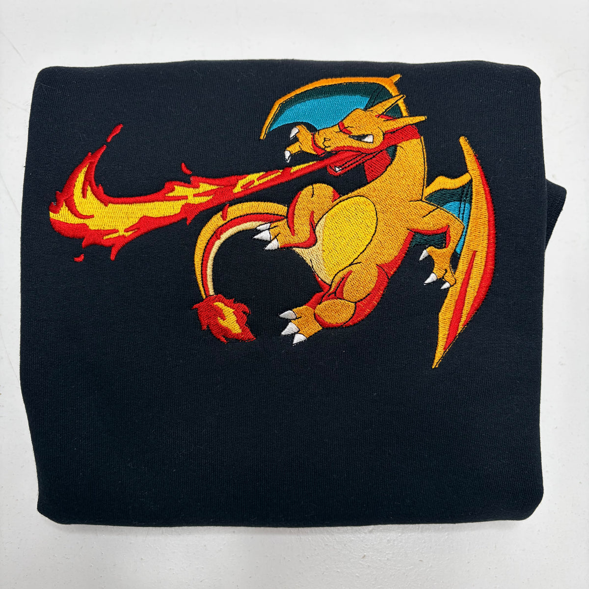 A folded black sweatshirt featuring a large embroidered Charizard graphic on the front, set against a plain white background.