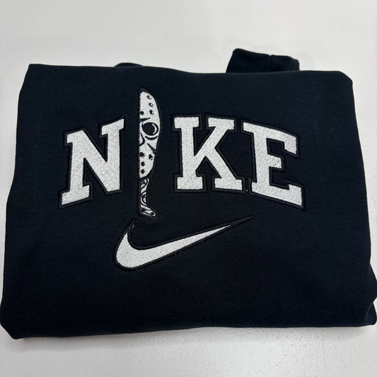 A folded black sweatshirt featuring a white embroidered 'NIKE' logo with a hockey player graphic for the 'I', and a white swoosh underneath, set against a plain light background.