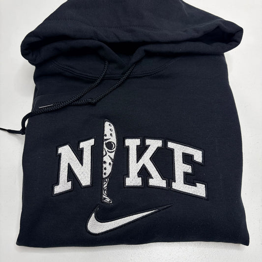 A folded black Nike hoodie with a white embroidered 'NIKE' logo and swoosh on the front, shown on a plain light background.