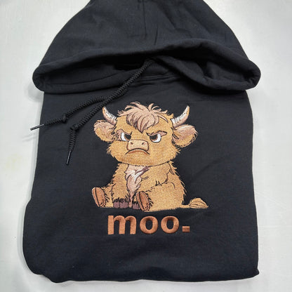A black hoodie featuring an embroidered Scottish highland cow character with the text 'moo-' embroidered below it, displayed on a light gray background.