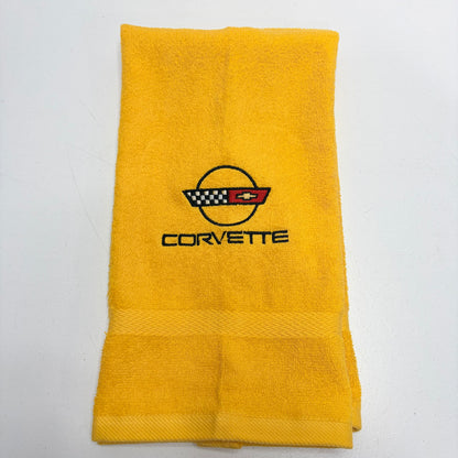 A folded yellow terry cloth towel featuring an embroidered Corvette logo and text in the center, set against a plain white background.