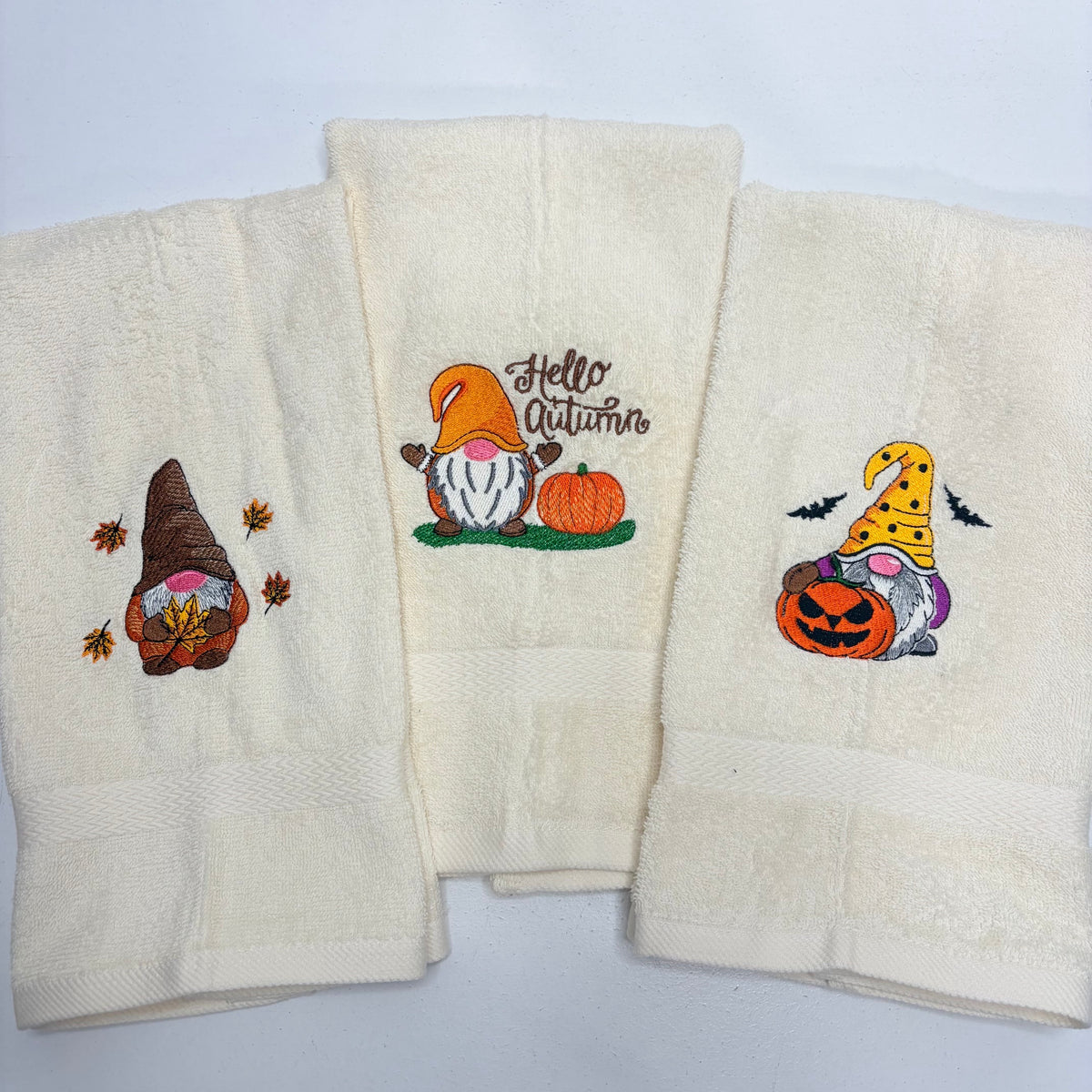 beige towels with embroidered fall gnome designs on them