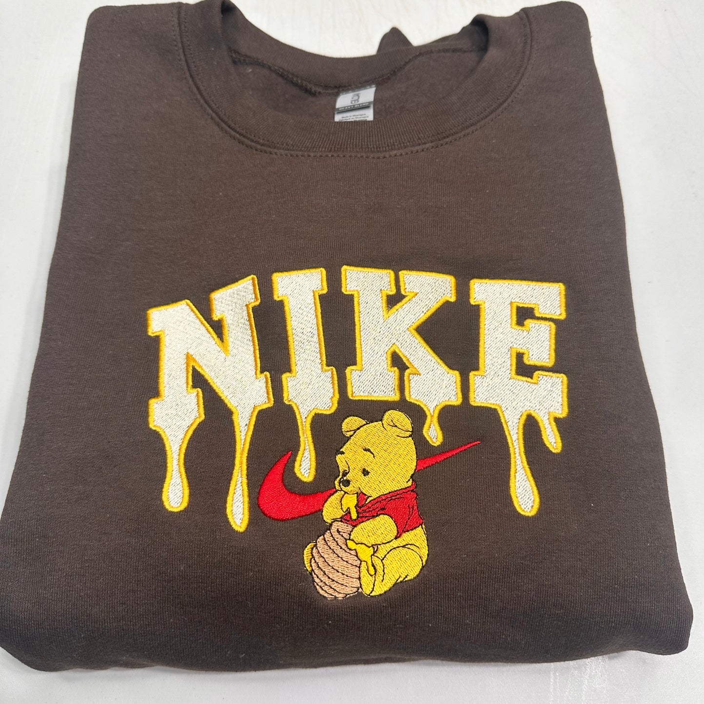 brown sweatshirt with embroidered winnie the pooh with honey dripping from the nike logo