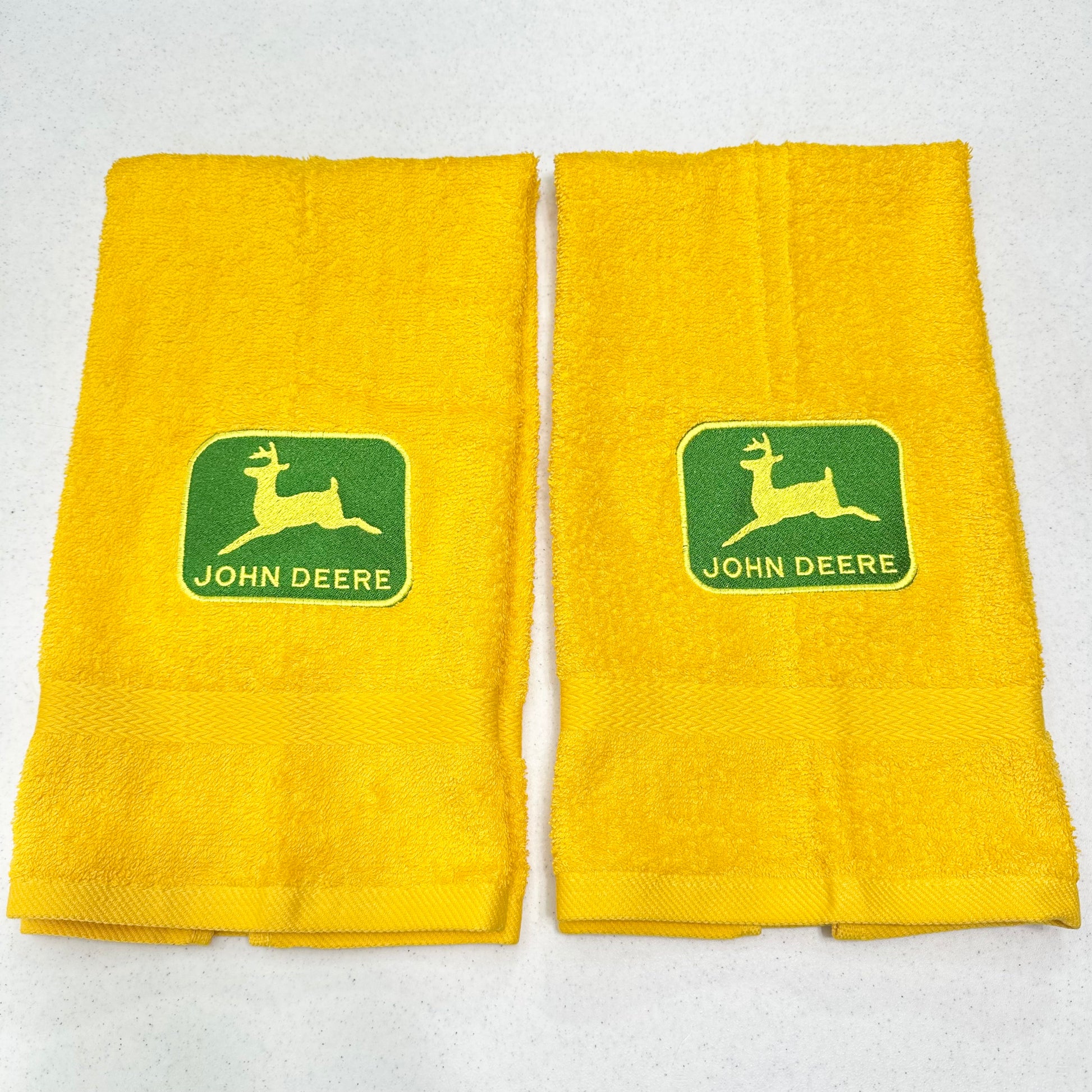 Two yellow towels with green John Deere logos, displayed side-by-side on a light gray background.