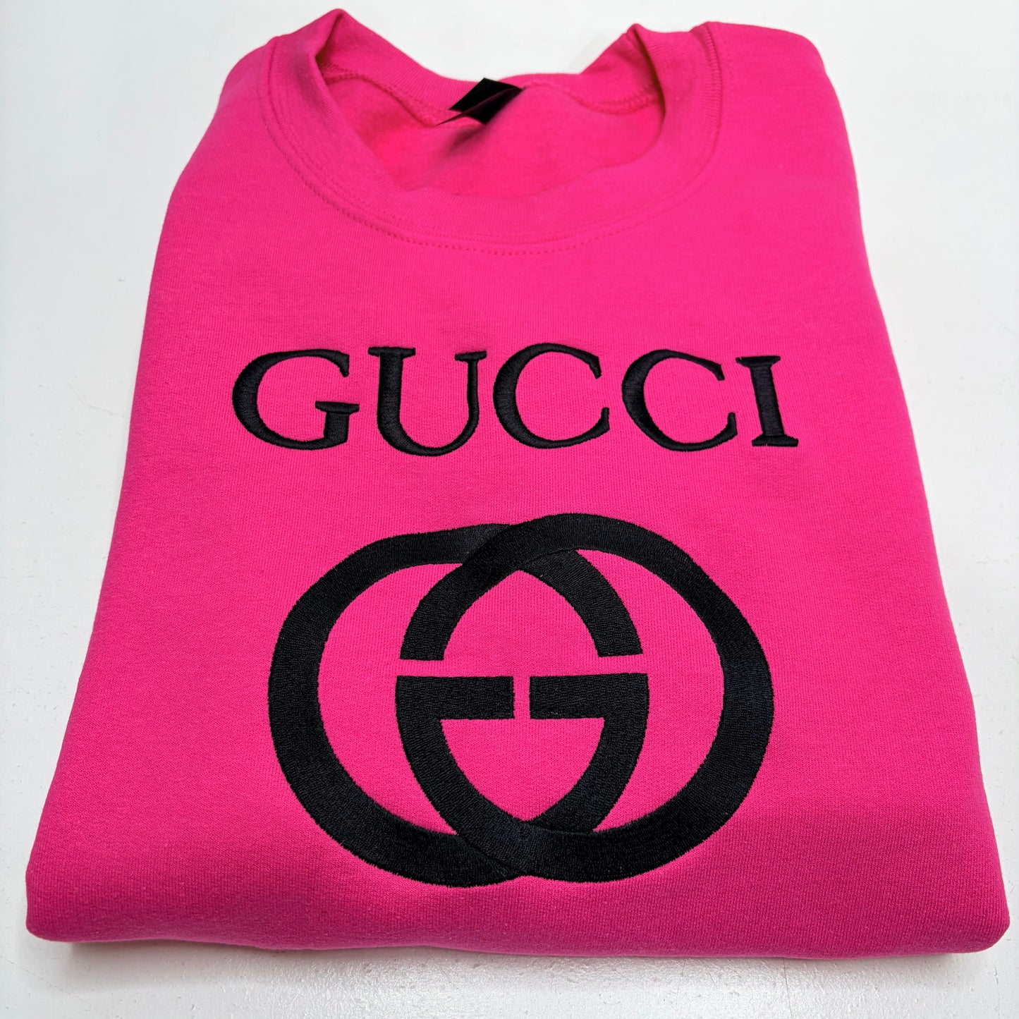 A folded hot pink sweatshirt featuring the black embroidered Gucci logo and interlocking GG emblem on the front, set against a plain white background.