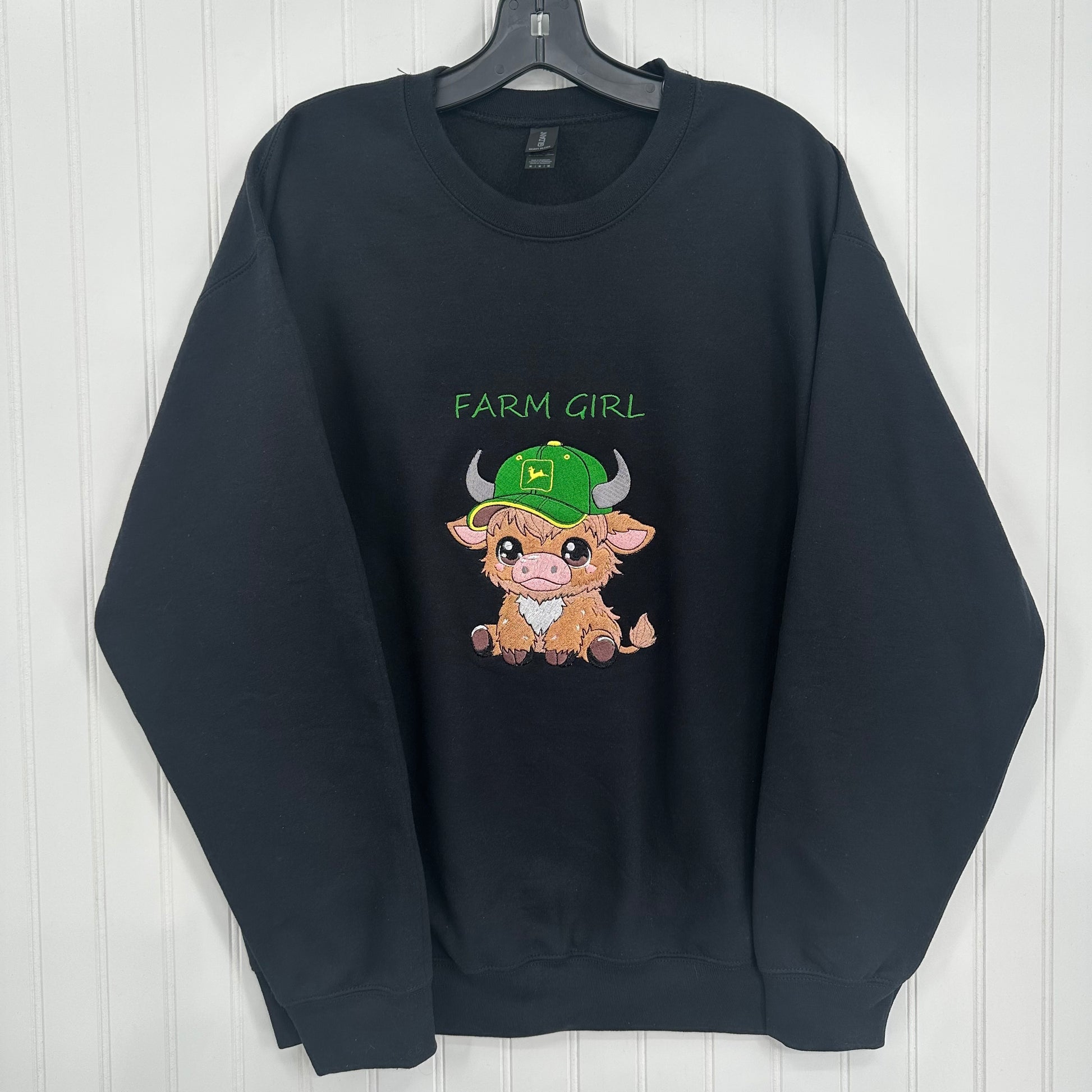 embroidered highland cow with green hat that says farm girl on a black sweatshirt