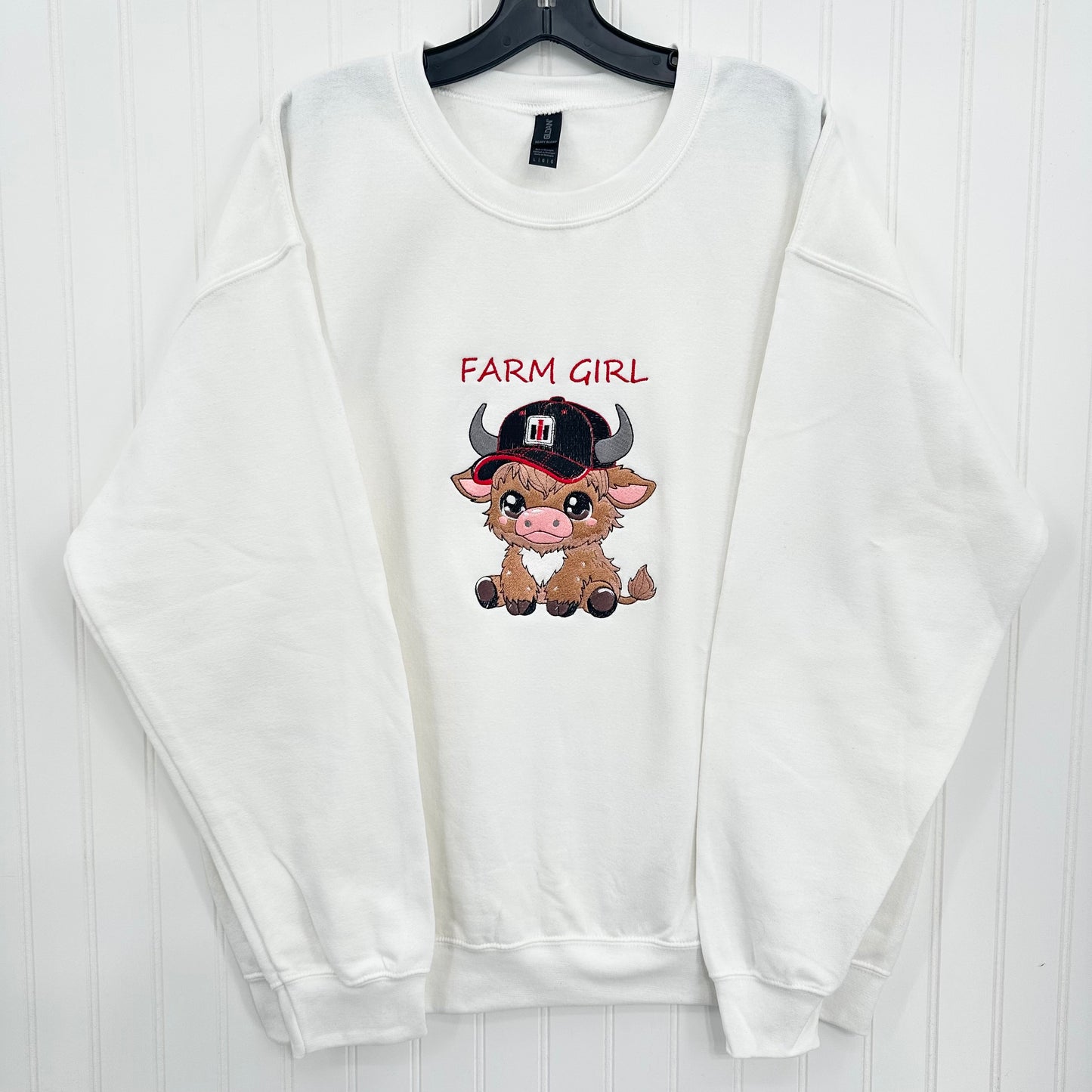 embroidered highland cow wearing a tractor hat on a white sweatshirt and says farm girl