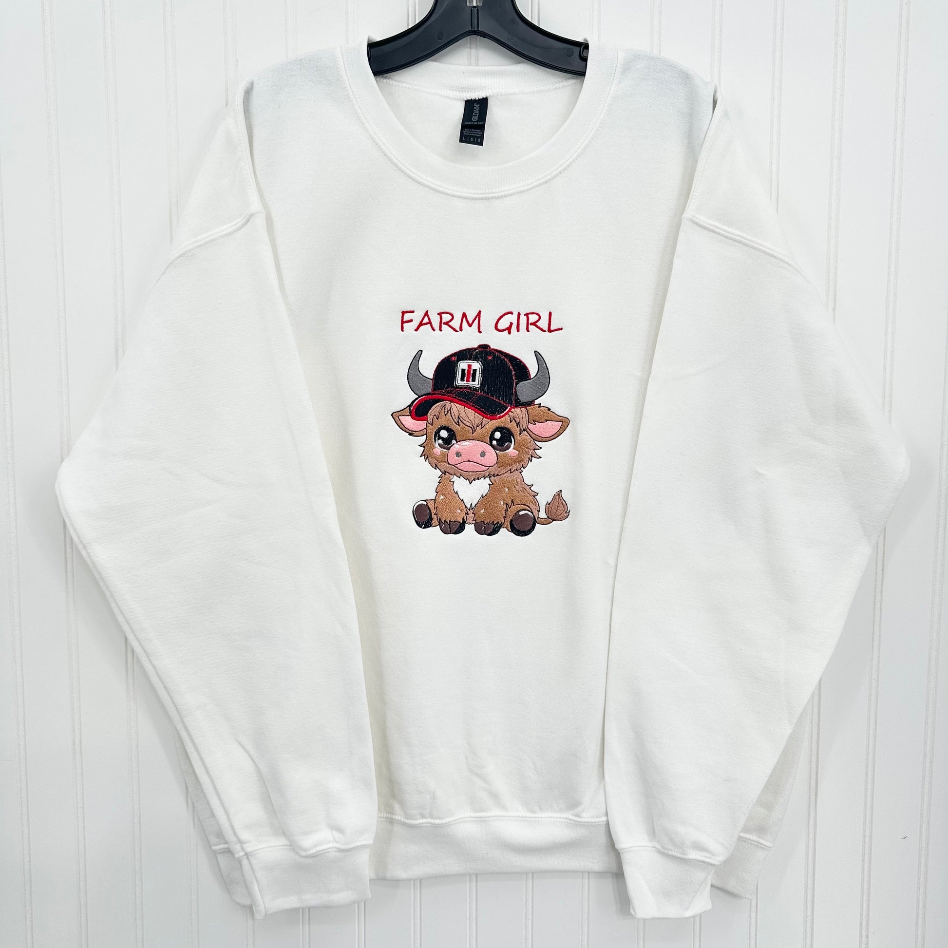 embroidered highland cow wearing a tractor hat on a white sweatshirt and says farm girl