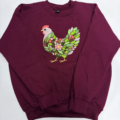 A maroon crewneck sweatshirt featuring a graphic of a chicken filled with green leaves and pink flowers on the chest, laid flat on a white background.