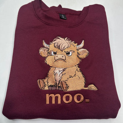 A folded maroon crewneck sweatshirt featuring a cartoon embroidered bull graphic with the text 'moo-' below it, displayed on a light gray background.