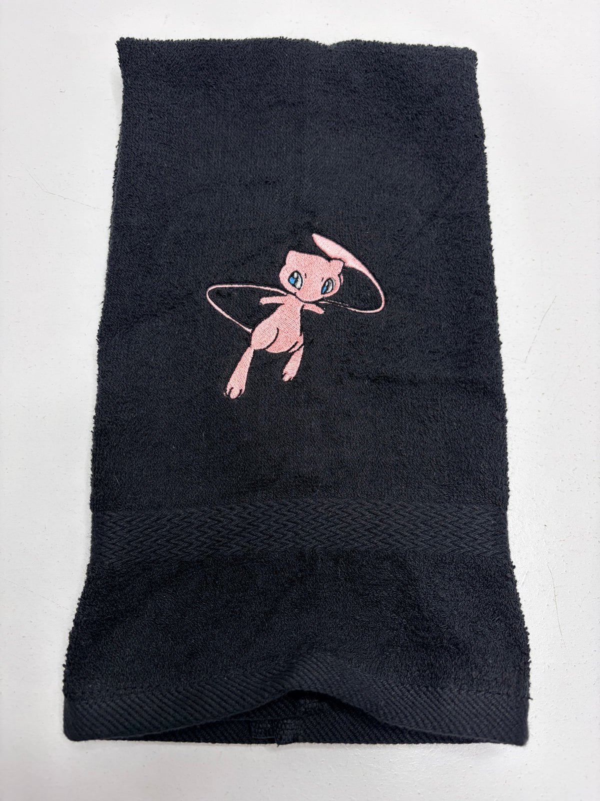black towel with pokemon mew character embroidered on it