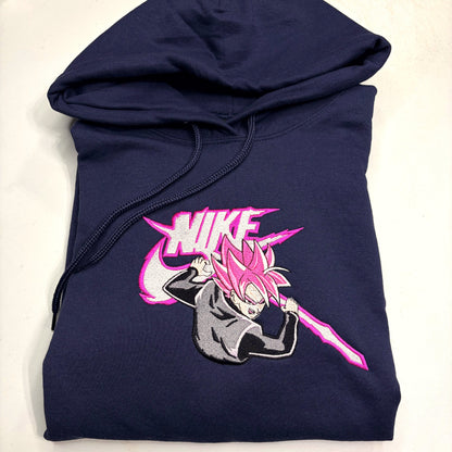 A navy blue hoodie featuring a large embroidered graphic of an anime character with pink hair and a pink sword, positioned in front of a stylized pink and white Nike logo.