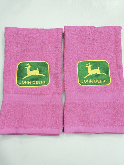 Two pink towels with green and yellow John Deere logos on the front, displayed side-by-side on a white background.