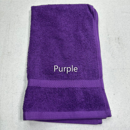 A folded purple terry cloth towel with a woven border and the word 'Purple' printed in white text in the center, laid flat on a light gray textured surface.