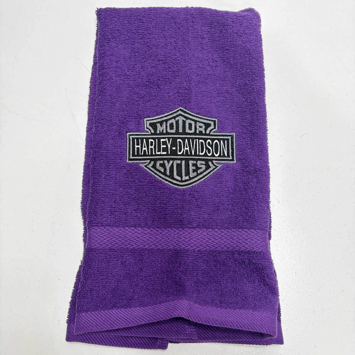 purple towel with an embroidered harley davidson logo in gray thread on it