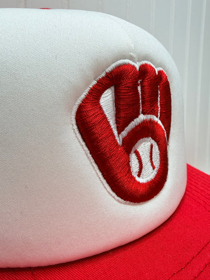 Close-up of a white baseball cap with a red embroidered logo featuring a baseball and a heart shape, with a red side panel visible.