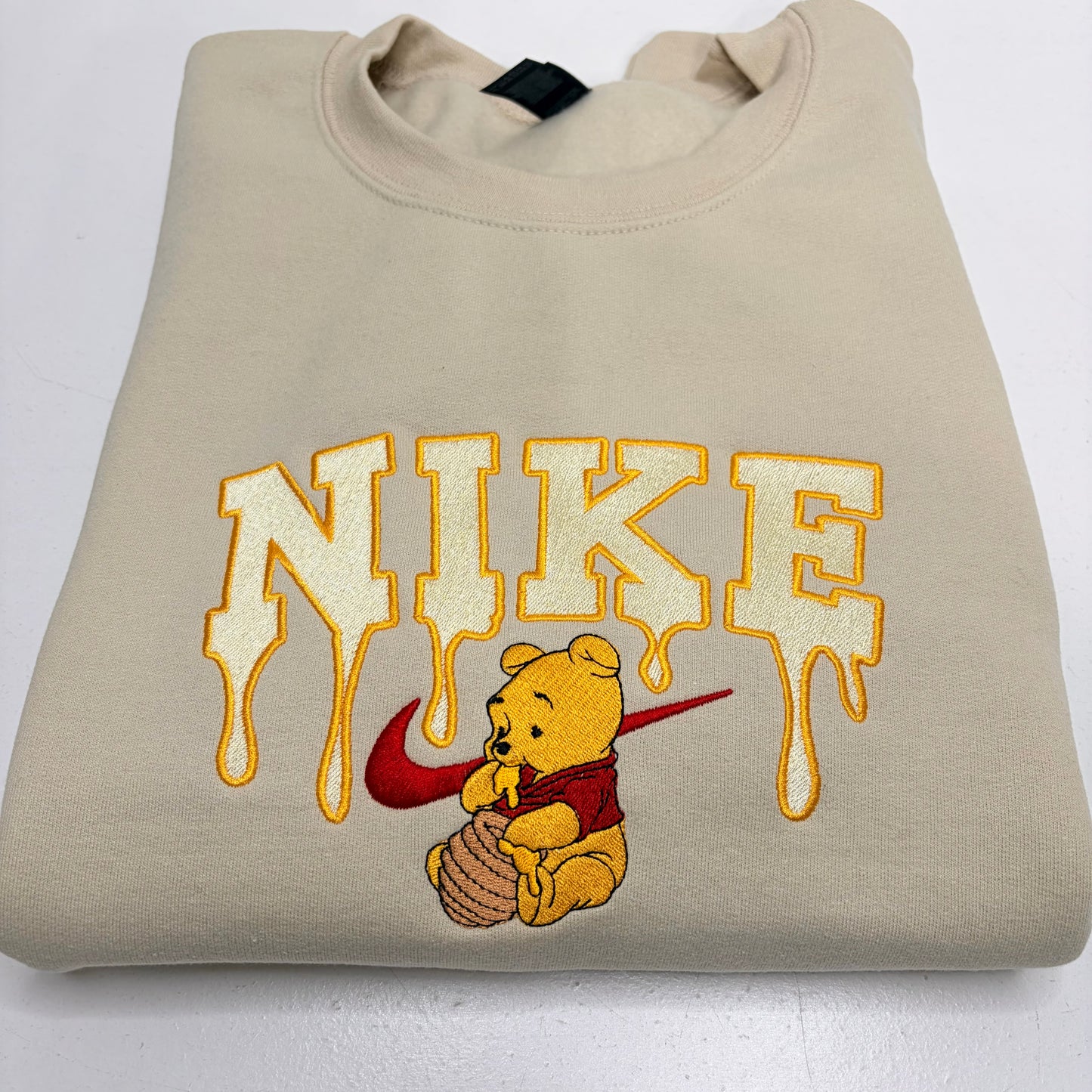 embroidered winnie the pooh with dripping honey nike logo on a beige sweatshirt