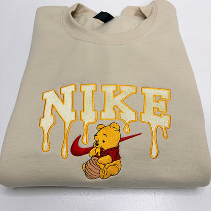 embroidered winnie the pooh with dripping honey nike logo on a beige sweatshirt
