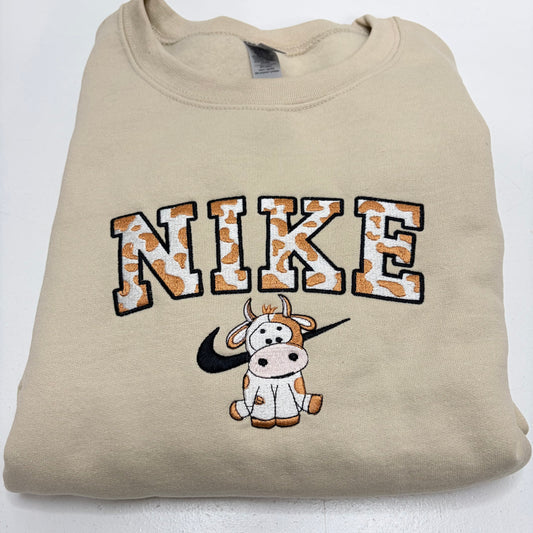 beige sweatshirt with an embroidered spotted cow in the nike logo