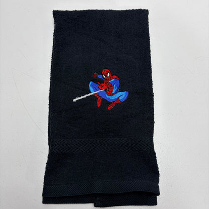 A folded black terry cloth towel featuring an embroidered Spider-Man character in red and blue with a web extending from his finger, set against a plain white background.