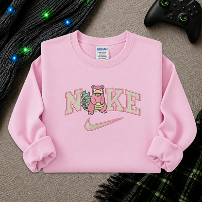 A pink long-sleeve sweatshirt laid flat on a textured gray surface, featuring a large 'Nike' graphic with a pink creature and a Nike swoosh. A Gildan brand tag is visible inside the collar.