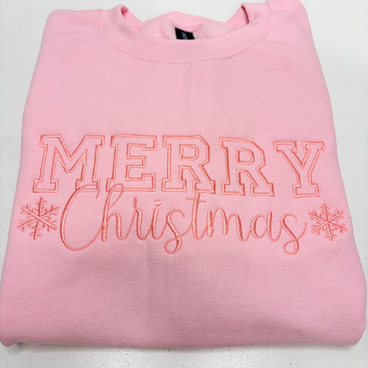 A folded light pink crewneck sweatshirt featuring 'MERRY Christmas' embroidered in pink thread with snowflake accents on the front.