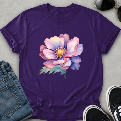 A purple short-sleeve crewneck t-shirt featuring a large watercolor-style pink and purple flower with green leaves on the front, styled in a flat lay with blue jeans, sunglasses, and black sneakers on a gray background.