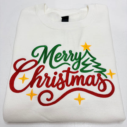 A folded white crewneck sweatshirt featuring a colorful embroidered 'Merry Christmas' design with a green tree and yellow stars on a white background.