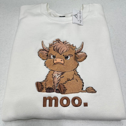 A folded white sweatshirt featuring a brown embroidered cartoon cow with the word 'moo.' underneath, shown on a light gray textured background.