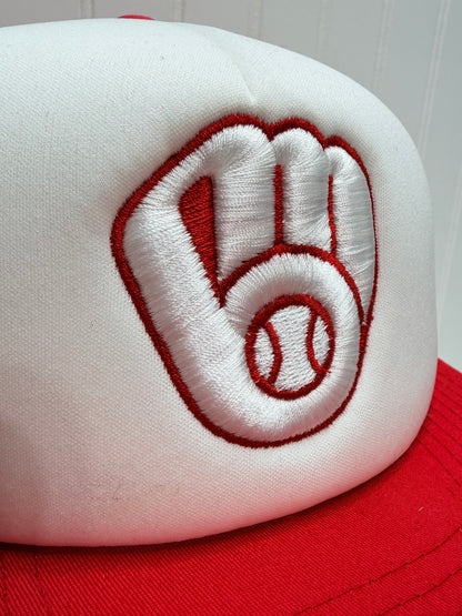 Close-up of a baseball cap's crown showing a white embroidered patch with a red outline of a baseball glove and baseball, next to red fabric.