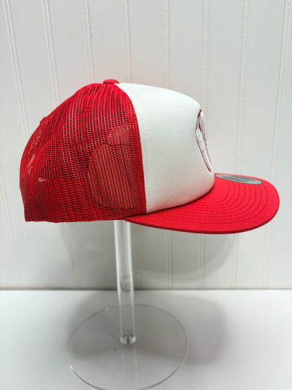 A red and white trucker-style baseball cap with a white front panel, red mesh back, and red flat brim, displayed on a clear acrylic stand against a white paneled background.