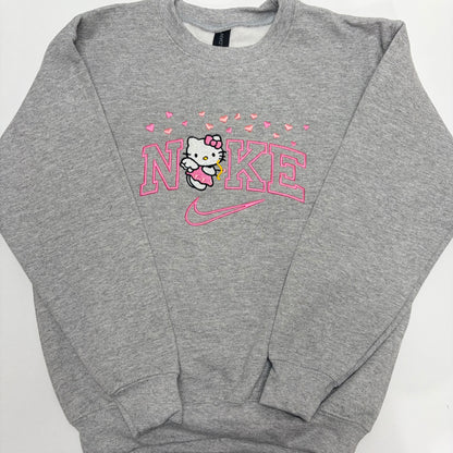 A heather gray crewneck sweatshirt featuring a pink and white Hello Kitty and Nike graphic on the chest, laid flat on a white background.