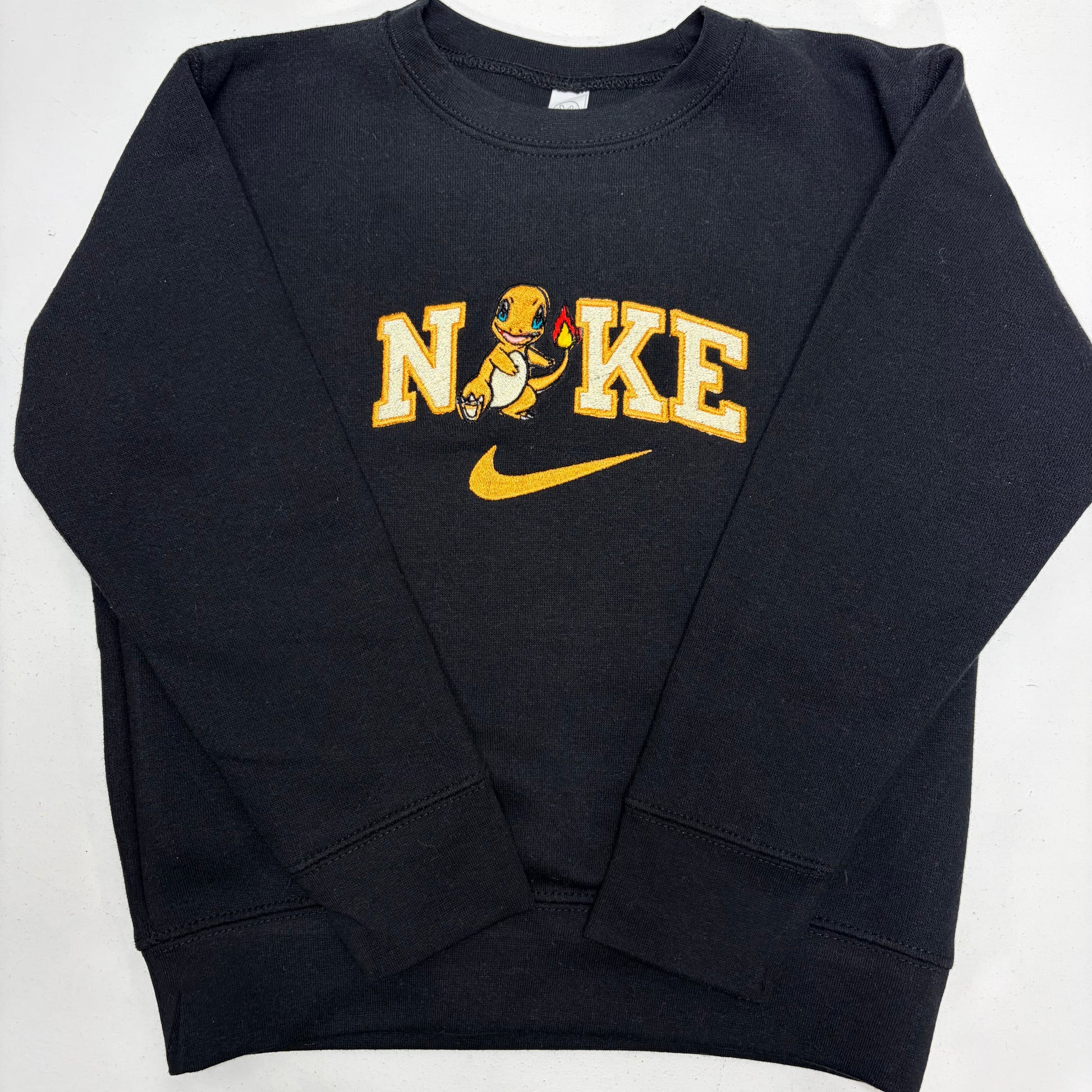 A black crewneck sweatshirt featuring a yellow and white 'NiKE' graphic with a cartoon pokemon charmander and a yellow Nike swoosh on the front, laid flat on a white background.